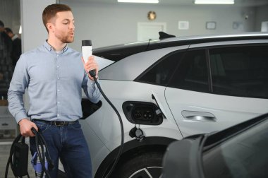 Elektrikli araba alma kavramı. Yakışıklı iş adamı galeride elektrikli arabanın yanında duruyor..