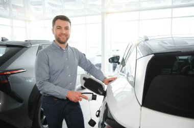 Delikanlı, galeride elektrikli araba satıyor. Aile için çevre dostu araba alma kavramı.