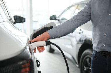 Sakallı adam yeni şarj kablosu deniyor. Araba galerisinde şarj istasyonu var. Elektrikli araba alma kavramı. Zeki ekolojik yaşam.