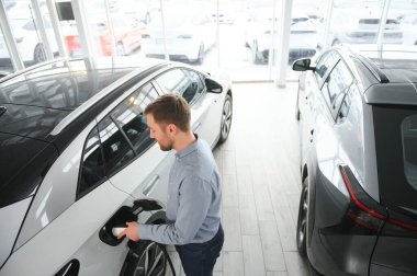 Elektrikli araba alma kavramı. Yakışıklı iş adamı galeride elektrikli arabanın yanında duruyor..