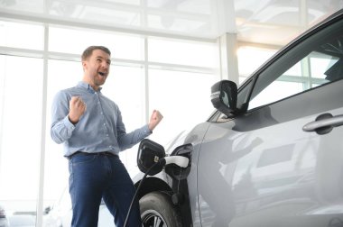 Sakallı adam yeni şarj kablosu deniyor. Araba galerisinde şarj istasyonu var. Elektrikli araba alma kavramı. Zeki ekolojik yaşam.