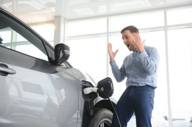 Sakallı adam yeni şarj kablosu deniyor. Araba galerisinde şarj istasyonu var. Elektrikli araba alma kavramı. Zeki ekolojik yaşam.