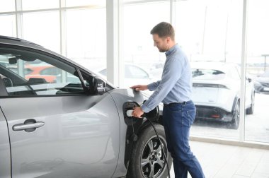 Elektrikli araba alma kavramı. Yakışıklı iş adamı galeride elektrikli arabanın yanında duruyor..
