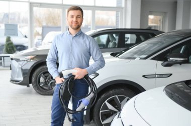 Mutlu bir adam bir araba galerisinde yeni bir elektrikli araba seçer. Ekolojik araba alma kavramı.