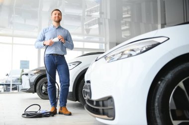 Delikanlı, galeride elektrikli araba satıyor. Aile için çevre dostu araba alma kavramı.