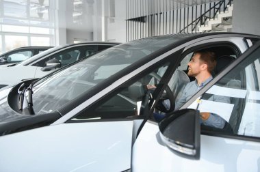 Mutlu bir adam bir araba galerisinde yeni bir elektrikli araba seçer. Ekolojik araba alma kavramı.