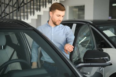 Genç bir adam araba galerisinde yeni bir araba seçiyor.