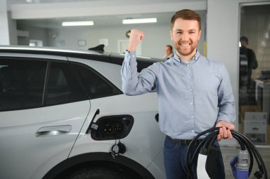 Elektrikli araba alma kavramı. Yakışıklı iş adamı galeride elektrikli arabanın yanında duruyor..