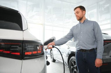 Elektrikli araba alma kavramı. Yakışıklı iş adamı galeride elektrikli arabanın yanında duruyor..