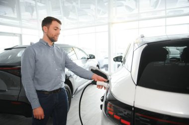 Sakallı adam yeni şarj kablosu deniyor. Araba galerisinde şarj istasyonu var. Elektrikli araba alma kavramı. Zeki ekolojik yaşam.