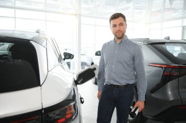 Elektrikli araba alma kavramı. Yakışıklı iş adamı galeride elektrikli arabanın yanında duruyor..