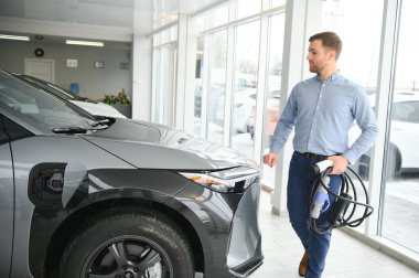Elektrikli araba alma kavramı. Yakışıklı iş adamı galeride elektrikli arabanın yanında duruyor..