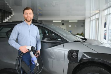 Elektrikli araba alma kavramı. Yakışıklı iş adamı galeride elektrikli arabanın yanında duruyor..