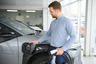 Delikanlı, galeride elektrikli araba satıyor. Aile için çevre dostu araba alma kavramı.