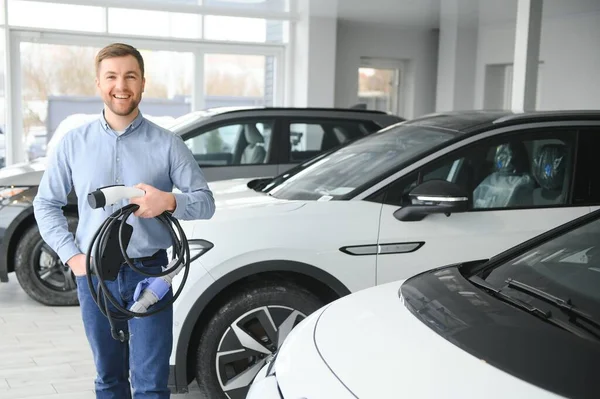 Sakallı adam yeni şarj kablosu deniyor. Araba galerisinde şarj istasyonu var. Elektrikli araba alma kavramı. Zeki ekolojik yaşam.