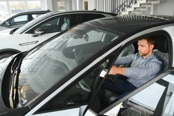 Mutlu bir adam bir araba galerisinde yeni bir elektrikli araba seçer. Ekolojik araba alma kavramı.