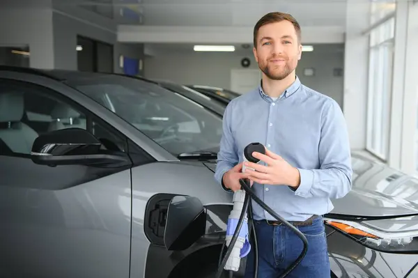 Young man buying first electric car in the showroom. Eco car sale concept.