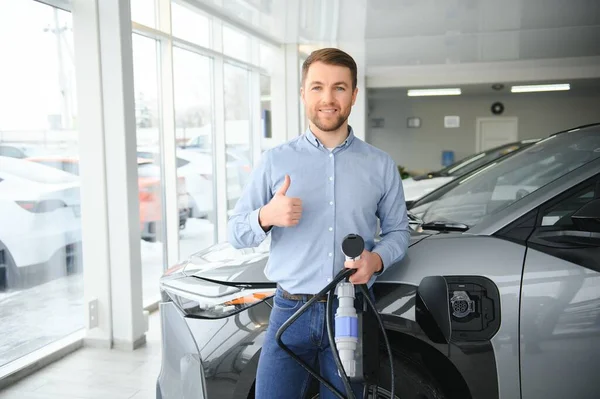 Sakallı adam yeni şarj kablosu deniyor. Araba galerisinde şarj istasyonu var. Elektrikli araba alma kavramı. Zeki ekolojik yaşam.