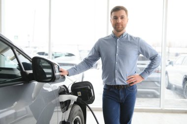 Elektrikli araba alma kavramı. Yakışıklı iş adamı galeride elektrikli arabanın yanında duruyor..