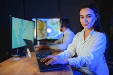 Ofiste bilgisayar kullanan, kulaklıklı, güler yüzlü bir kadın çağrı merkezi operatörü..