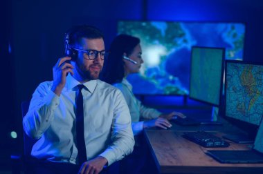 Oda izleme içinde teknik destek uzmanı kulaklık konuşuyor. Onun meslektaşları arka planda çalışan.