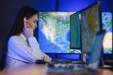 Ofiste bilgisayar kullanan, kulaklıklı, güler yüzlü bir kadın çağrı merkezi operatörü..