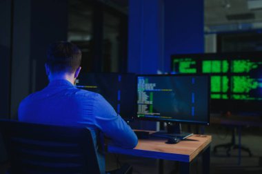 Beyaz masadaki masaüstü bilgisayarında çalışan erkek programcı.