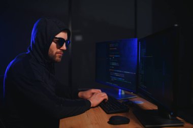 Bilgisayar korsanı karanlık atmosferde masada oturuyor. Bilgisayar programcısı ya da hacker. Anonim bilgisayar korsanı. Karanlık odada bilgisayar korsanı