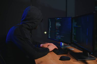 Bilgisayar korsanı karanlık atmosferde masada oturuyor. Bilgisayar programcısı ya da hacker. Anonim bilgisayar korsanı. Karanlık odada bilgisayar korsanı