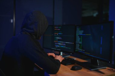 Bilgisayar korsanı karanlık atmosferde masada oturuyor. Bilgisayar programcısı ya da hacker. Anonim bilgisayar korsanı. Karanlık odada bilgisayar korsanı