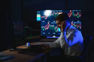 Ofis masasında oturan kripto simsarının yan görünüşü, pazarı analiz etmek, ekrana bakmak..