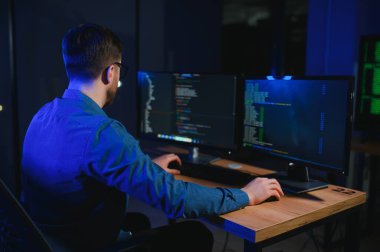 Beyaz masadaki masaüstü bilgisayarında çalışan erkek programcı.