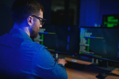 Beyaz masadaki masaüstü bilgisayarında çalışan erkek programcı.