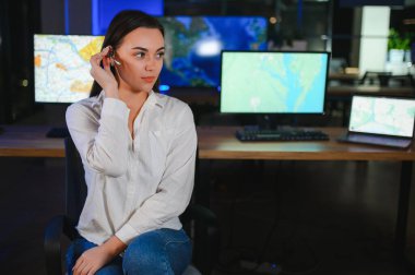 Ofiste bilgisayar kullanan, kulaklıklı, güler yüzlü bir kadın çağrı merkezi operatörü..