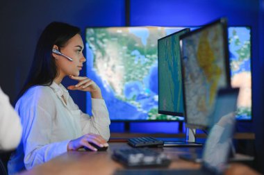 Ofiste bilgisayar kullanan, kulaklıklı, güler yüzlü bir kadın çağrı merkezi operatörü..