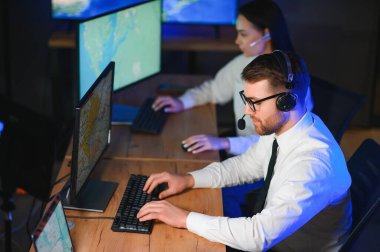 Oda izleme içinde teknik destek uzmanı kulaklık konuşuyor. Onun meslektaşları arka planda çalışan.