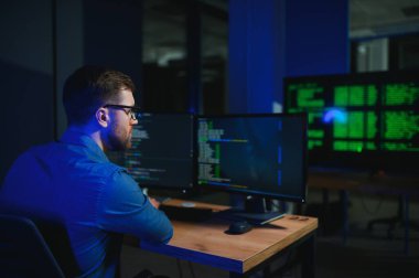 Beyaz masadaki masaüstü bilgisayarında çalışan erkek programcı.