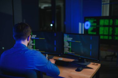 Gece Ofisi: Masaüstü Bilgisayarında Çalışan Genç Yakışıklı Adam. Dijital Girişimci Daktilo Kodu, Modern Yazılım Geliştirme, E-Ticari Uygulama Tasarımı, E-İş Geliştirme. Omuz üstünden.