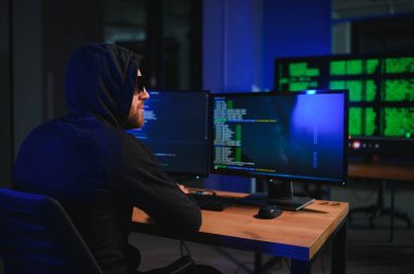 Bilgisayar korsanı karanlık atmosferde masada oturuyor. Bilgisayar programcısı ya da hacker. Anonim bilgisayar korsanı. Karanlık odada bilgisayar korsanı