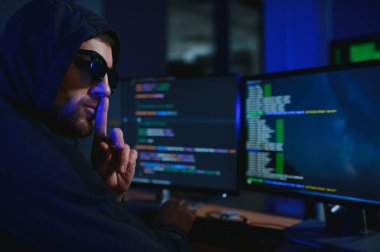 Bilgisayar korsanı karanlık atmosferde masada oturuyor. Bilgisayar programcısı ya da hacker. Anonim bilgisayar korsanı. Karanlık odada bilgisayar korsanı