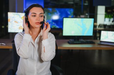 Ofiste bilgisayar kullanan, kulaklıklı, güler yüzlü bir kadın çağrı merkezi operatörü..