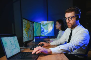 Oda izleme içinde teknik destek uzmanı kulaklık konuşuyor. Onun meslektaşları arka planda çalışan.