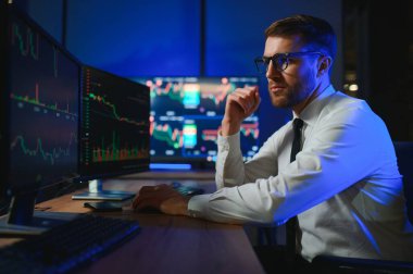 Ofis masasında oturan kripto simsarının yan görünüşü, pazarı analiz etmek, ekrana bakmak..