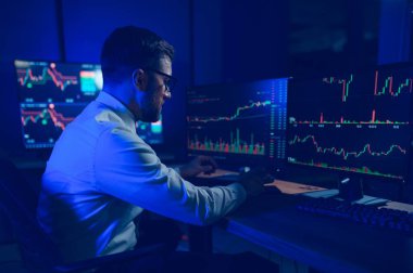 Ofis masasında oturan kripto simsarının yan görünüşü, pazarı analiz etmek, ekrana bakmak..