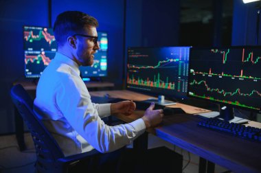 Ofis masasında oturan kripto simsarının yan görünüşü, pazarı analiz etmek, ekrana bakmak..