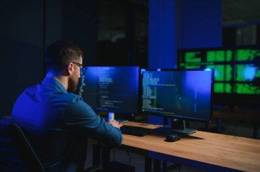 Gece Ofisi: Masaüstü Bilgisayarında Çalışan Genç Yakışıklı Adam. Dijital Girişimci Daktilo Kodu, Modern Yazılım Geliştirme, E-Ticari Uygulama Tasarımı, E-İş Geliştirme. Omuz üstünden.