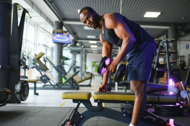 Genç Afrikalı Amerikalı bir adam spor salonunun rafına bir dambıl kaldırıyor..