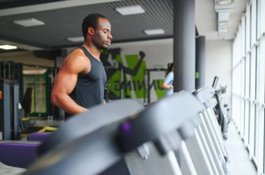 Sportive black man exercising on treadmill in fitness club.