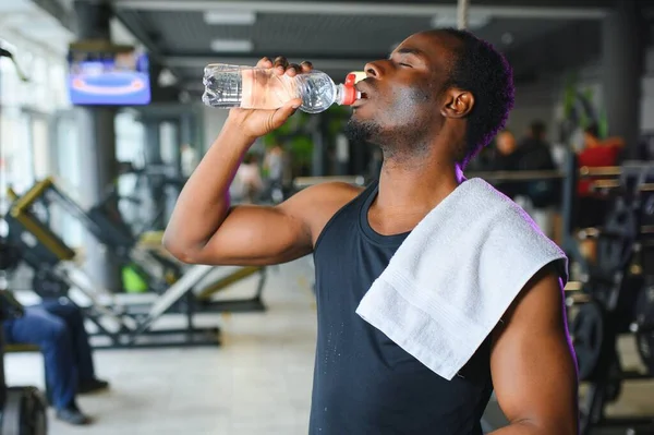 African american bodybuilder holding mug with water at modern gym.