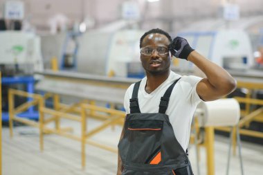 Üniformalı ve endüstriyel fabrikada ayakta duran Afrikalı Amerikalı erkek mühendisin portresi.